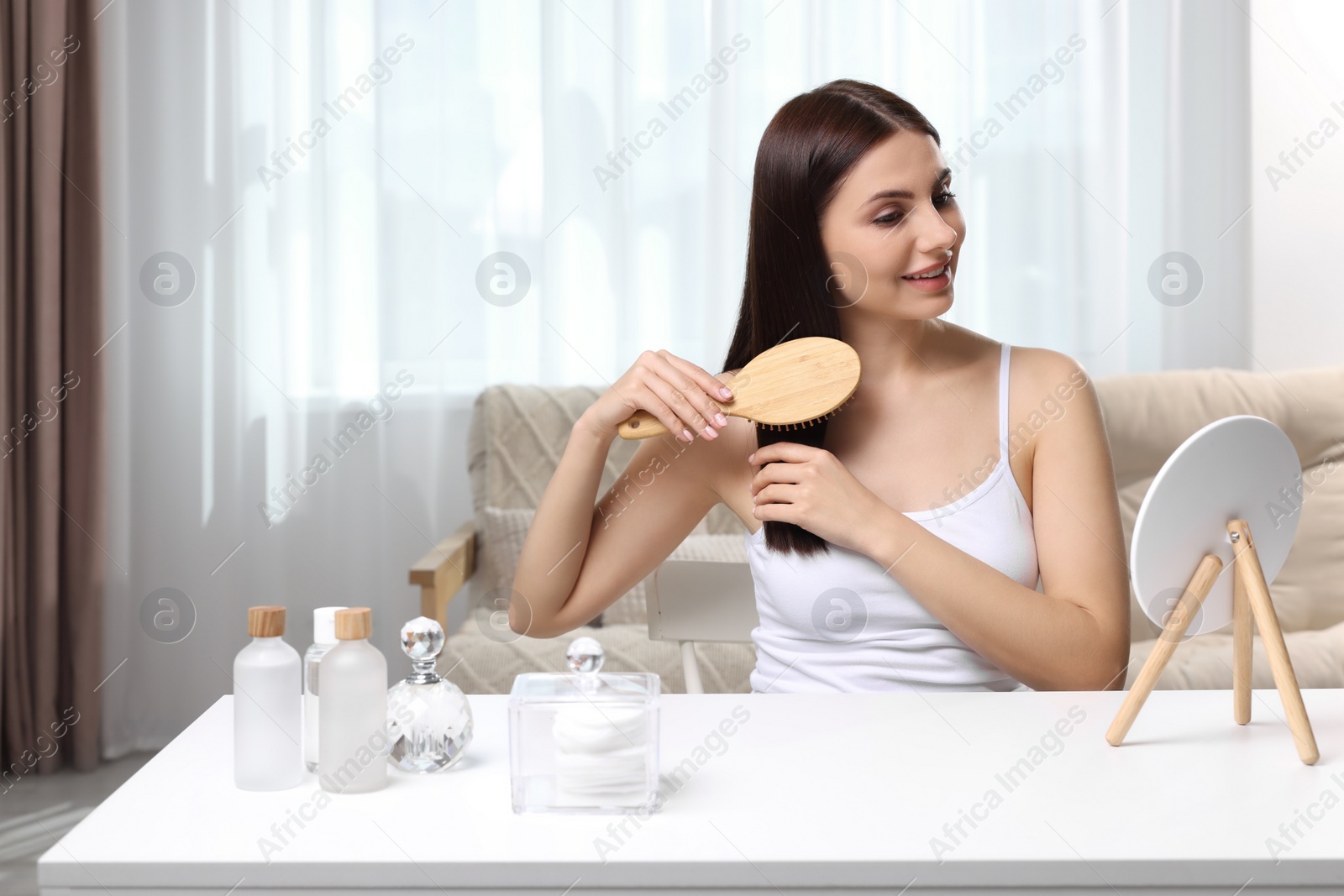 Photo of Beautiful woman brushing her hair near mirror in room, space for text