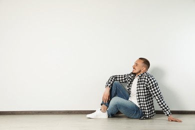 Photo of Handsome young man sitting on floor near white wall indoors, space for text