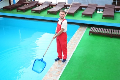 Photo of Male worker cleaning outdoor pool with scoop net