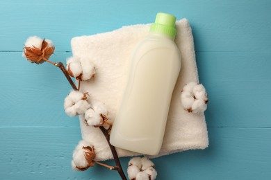 Photo of Bottle of fabric softener, terry towel and cotton flowers on light blue wooden table, flat lay