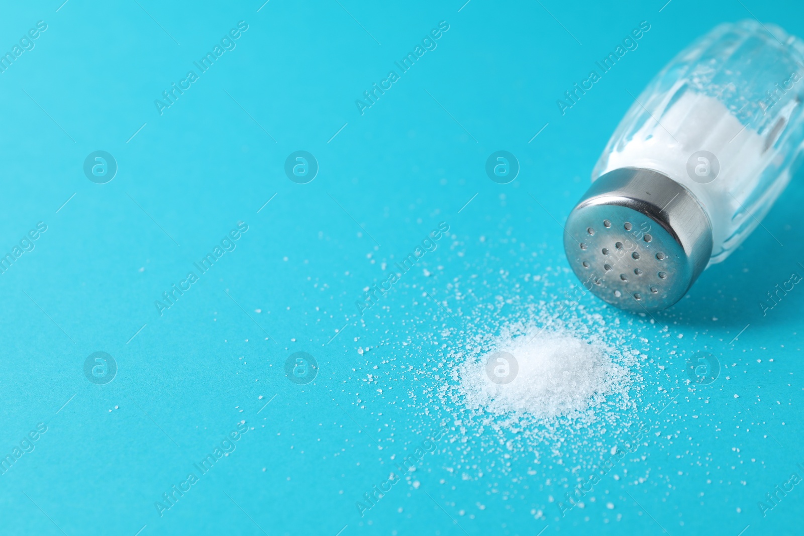 Photo of Organic white salt in glass shaker on light blue background, closeup. Space for text