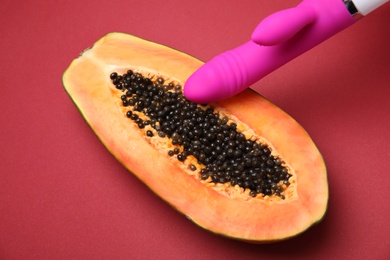 Photo of Half of papaya and purple vibrator on red background, above view. Sex concept