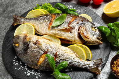 Photo of Delicious roasted fish with lemon on grey table