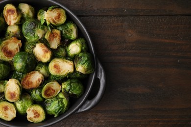 Photo of Delicious roasted Brussels sprouts in baking dish on wooden table, top view. Space for text