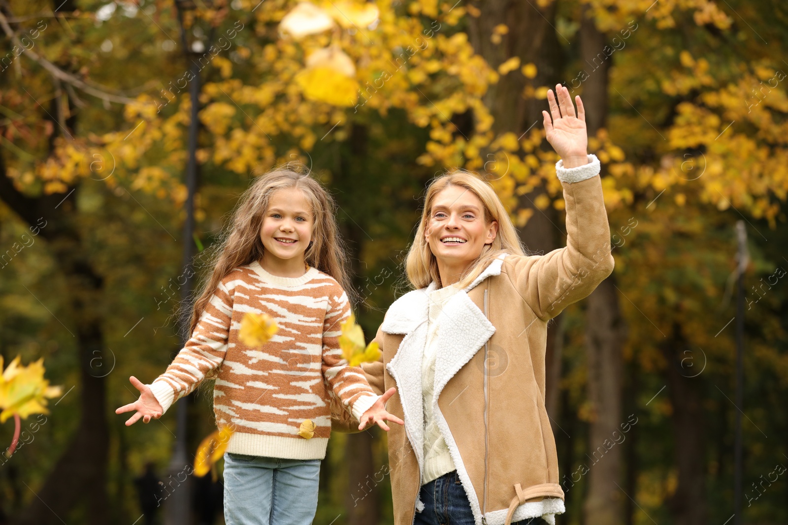 Photo of Happy mother and her daughter playing with dry leaves in autumn park