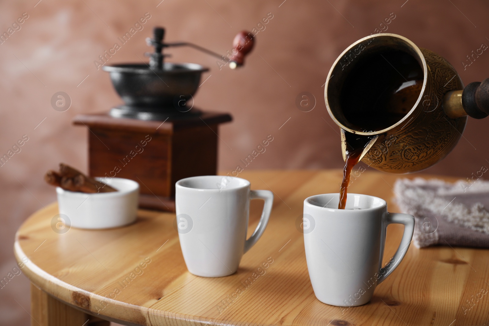 Photo of Turkish coffee. Pouring brewed beverage from cezve into cup at wooden table, closeup
