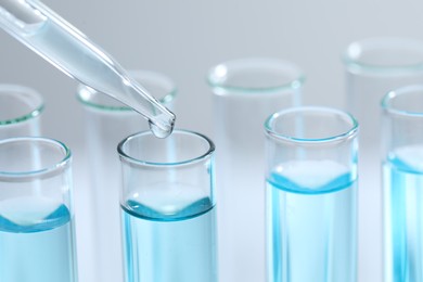 Photo of Dripping liquid from pipette into test tube on light background, closeup