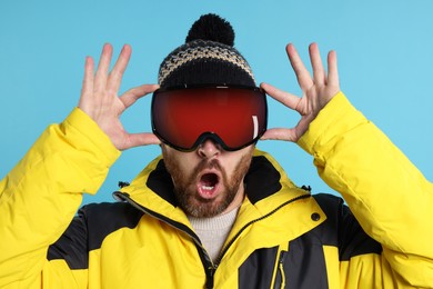 Photo of Winter sports. Emotional man in ski suit and goggles on light blue background