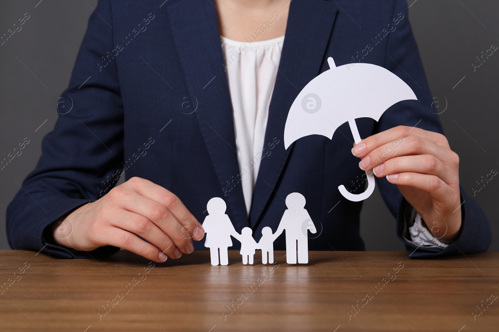 Photo of Woman holding cutout paper family and umbrella at table, closeup. Life insurance concept