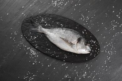 Photo of Fresh raw dorado fish and sea salt on black table, flat lay