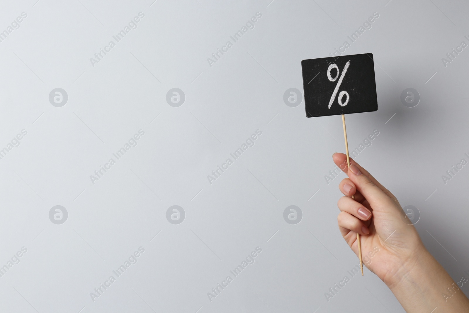 Photo of Woman holding sign with percent symbol on grey background, closeup. Space for text