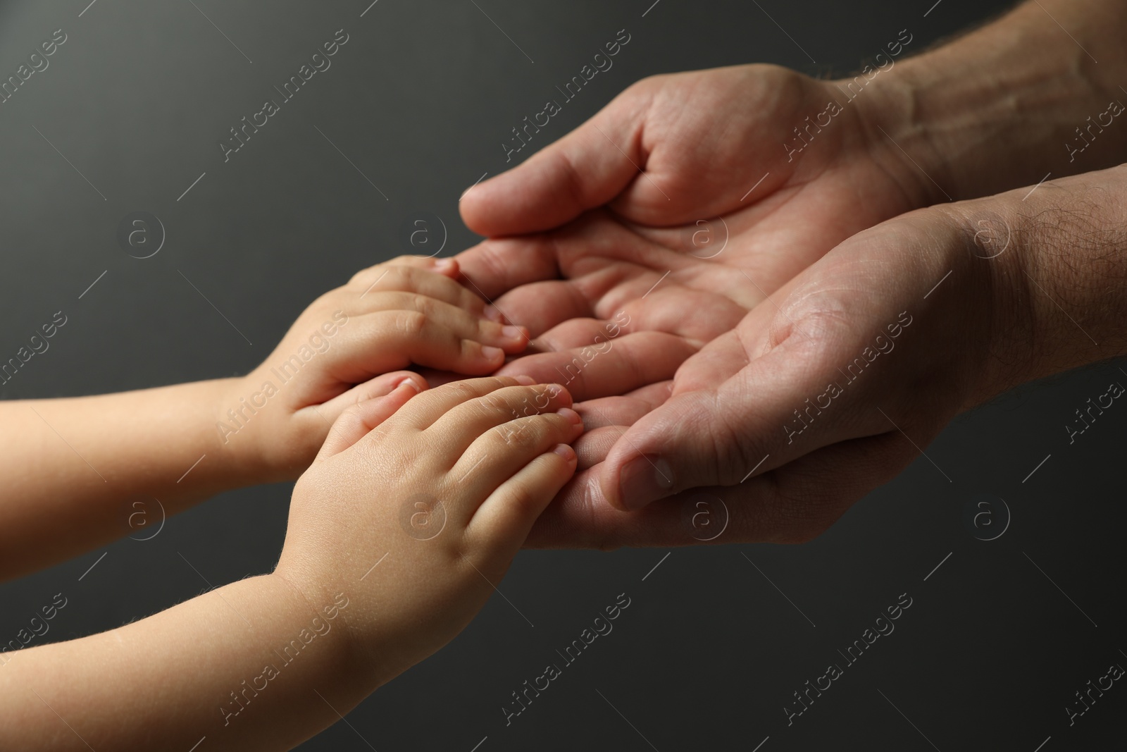 Photo of Father and child holding hands on dark grey background, closeup