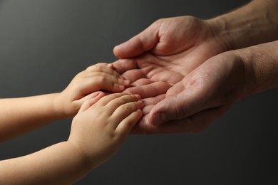 Father and child holding hands on dark grey background, closeup