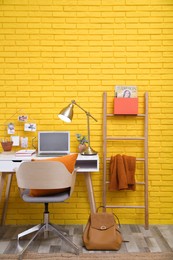 Stylish home office interior with comfortable workplace near yellow brick wall