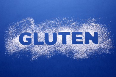 Photo of Word Gluten written with flour on blue background, top view