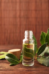 Bottle of bay essential oil and fresh leaves on wooden table