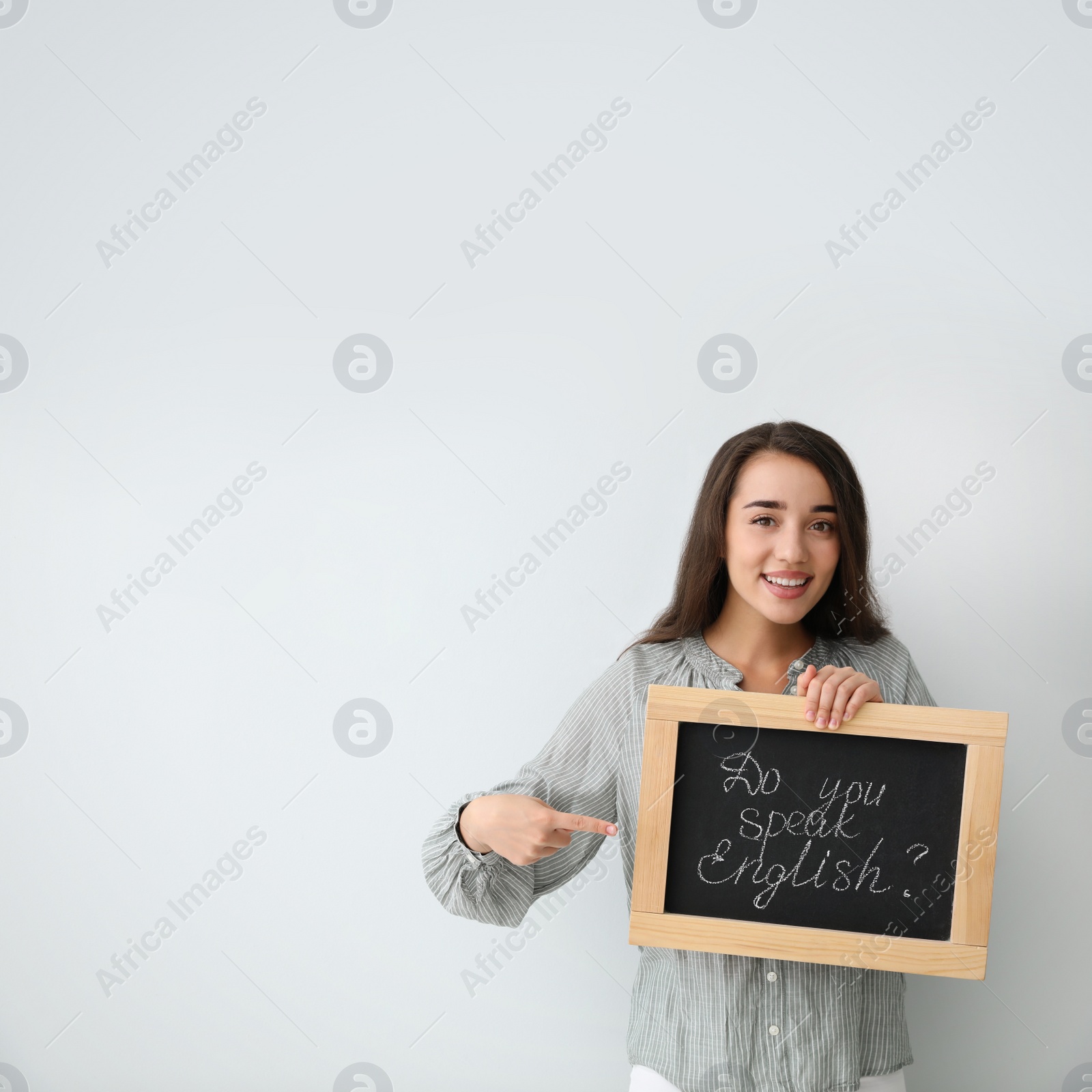 Photo of Young female teacher holding chalkboard with words DO YOU SPEAK ENGLISH? on light background. Space for text