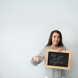 Photo of Young female teacher holding chalkboard with words DO YOU SPEAK ENGLISH? on light background. Space for text