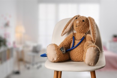 Image of Toy rabbit with stethoscope on chair indoors, space for text. Pediatrician practice