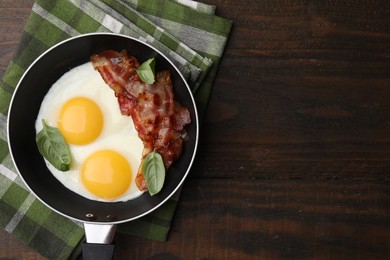 Photo of Fried eggs, bacon and basil in frying pan on wooden table, top view. Space for text