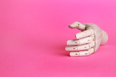 Photo of Wooden mannequin hand on pink background. Space for text