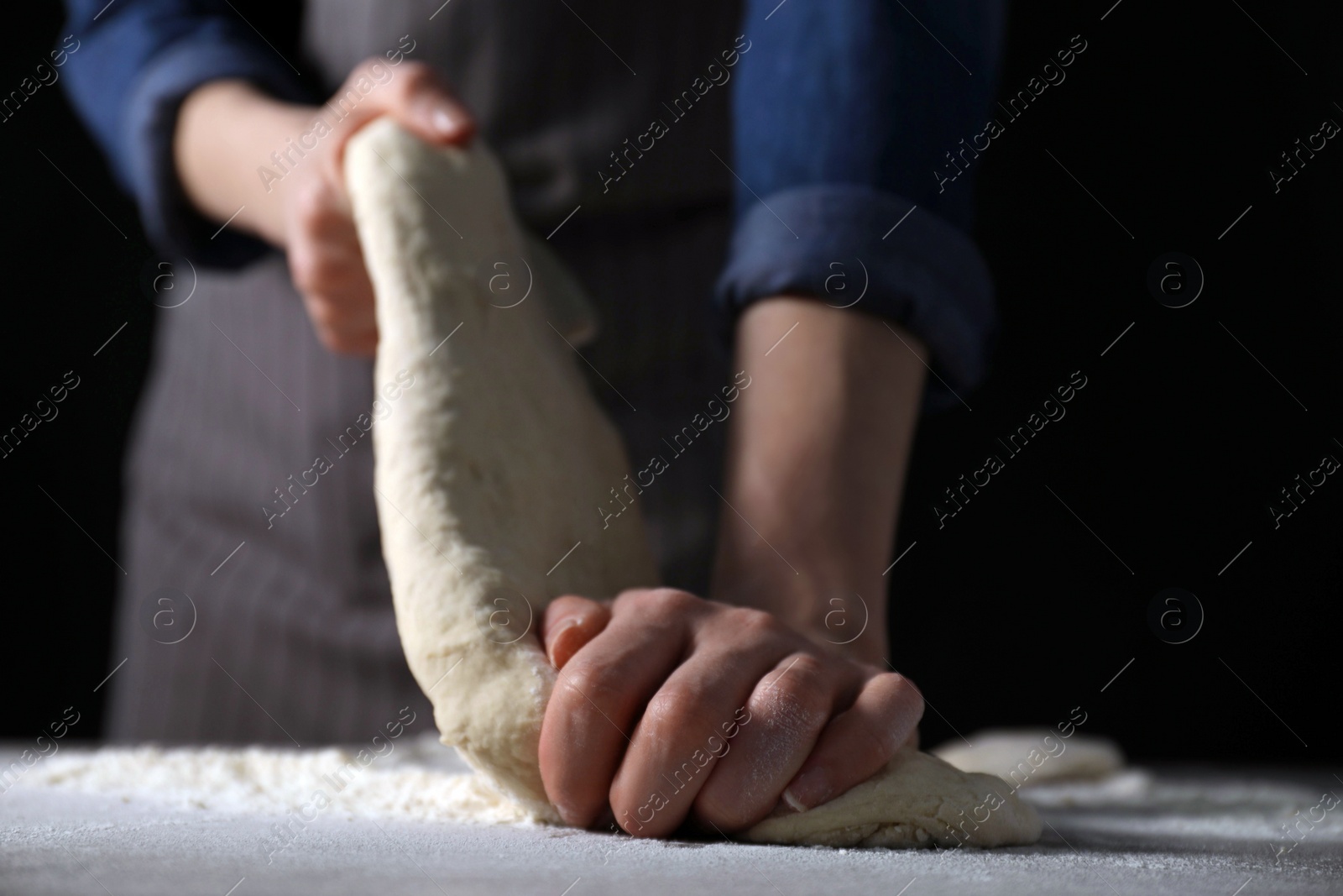 Photo of Making bread. Woman kneading dough at table on dark background, closeup