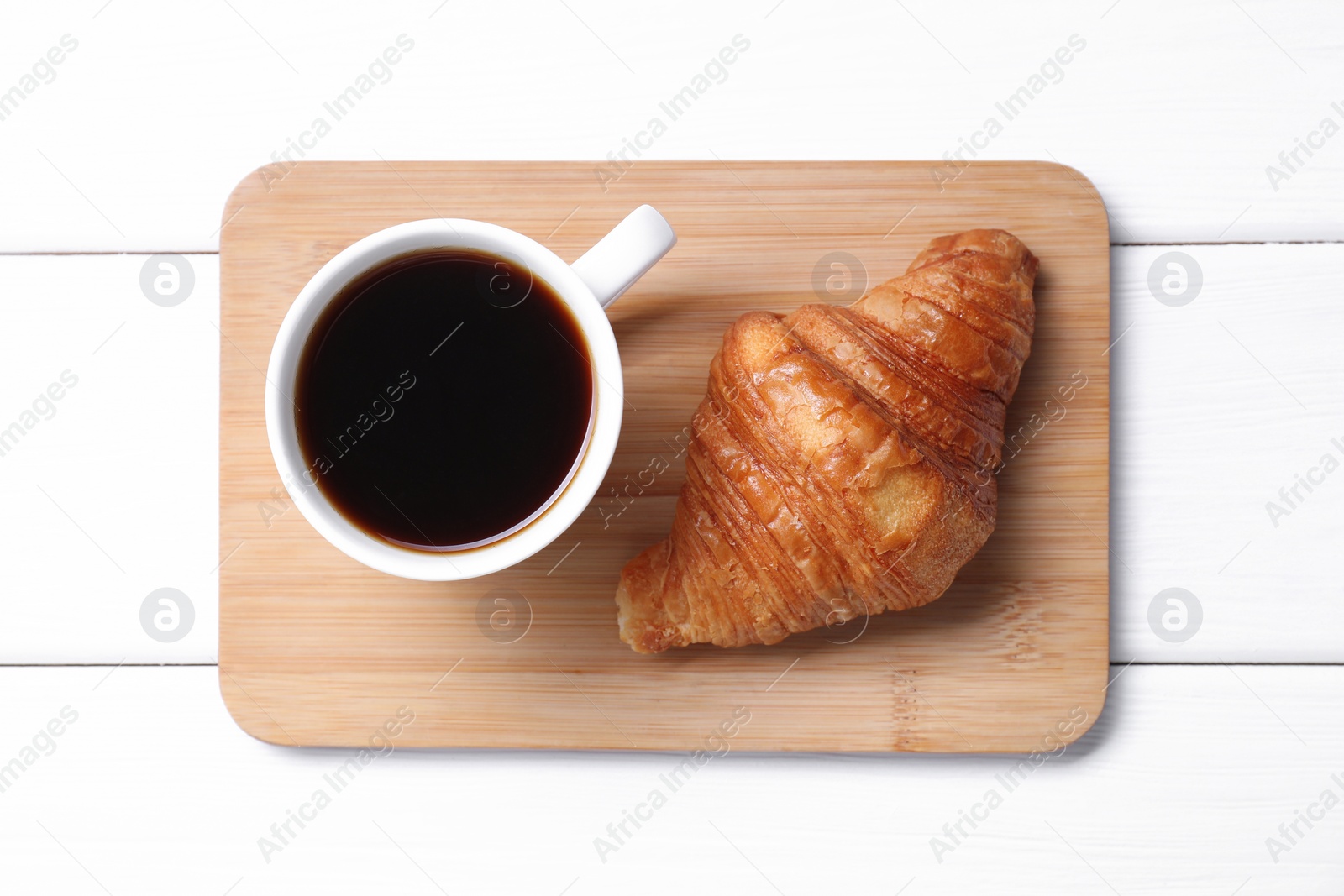 Photo of Tasty breakfast. Cup of coffee and croissant on white wooden table, top view