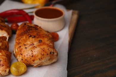 Photo of Baked chicken fillets and marinade on wooden table, closeup. Space for text