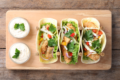 Yummy fish tacos served on wooden table, top view