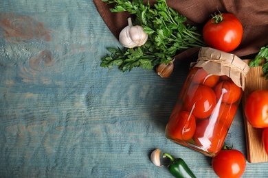 Flat lay composition with pickled tomatoes in glass jar on blue wooden table, space for text