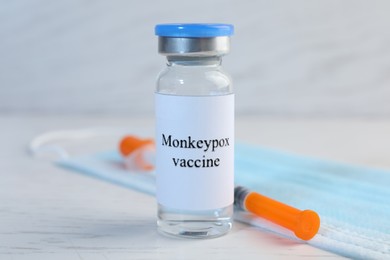 Monkeypox vaccine in glass vial, medical mask and syringe on white wooden table