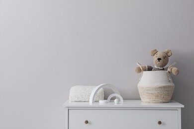 Child's toys, wicker basket and plaid on chest of drawers near light grey wall indoors. Space for text