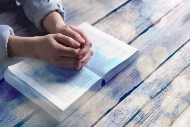 Religion. Christian woman praying over Bible at table, closeup. Bokeh effect