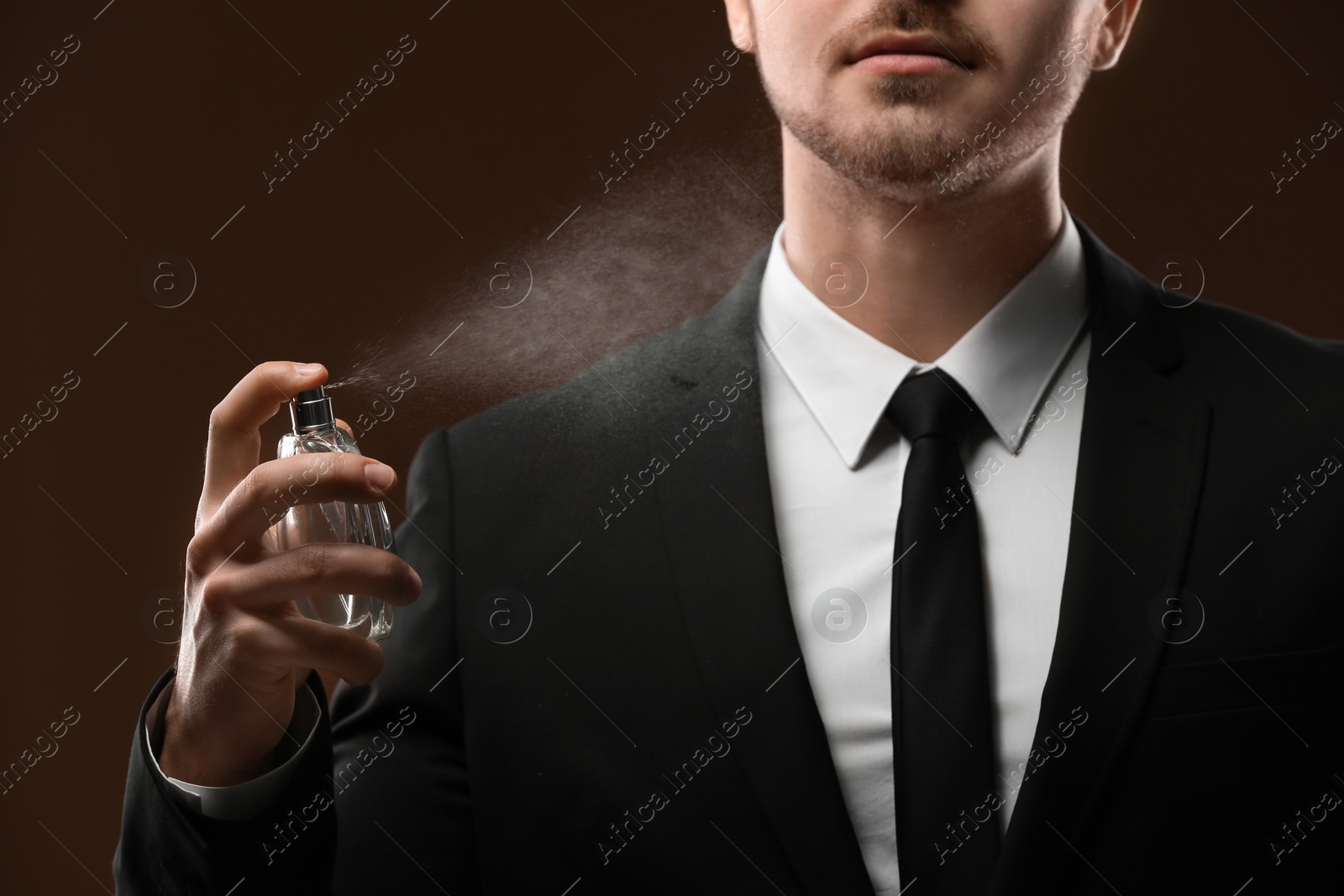 Photo of Handsome man in suit using perfume on dark background, closeup