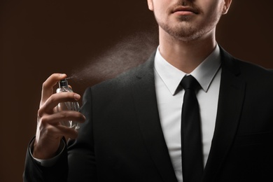 Photo of Handsome man in suit using perfume on dark background, closeup