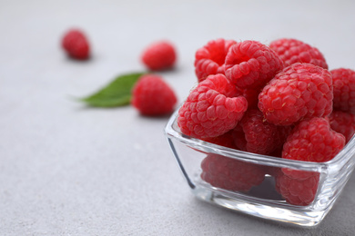 Photo of Delicious fresh ripe raspberries in glass bowl on grey table, closeup. Space for text