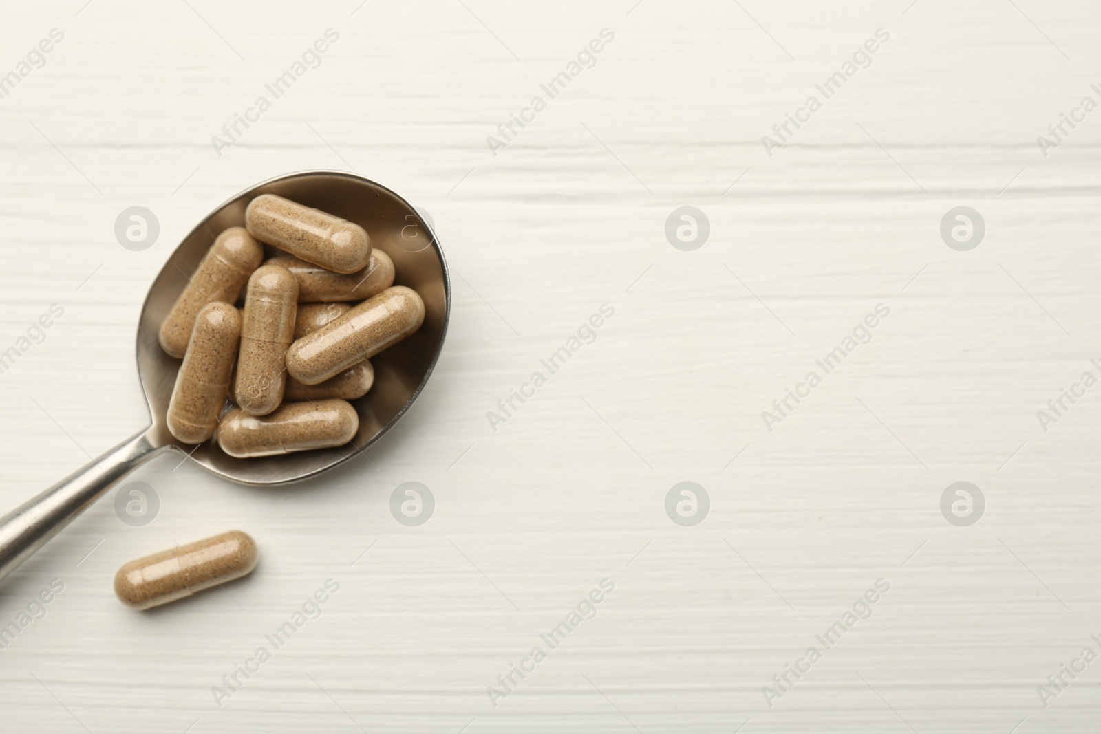 Photo of Vitamin capsules in spoon on white wooden table, top view. Space for text