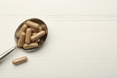 Vitamin capsules in spoon on white wooden table, top view. Space for text