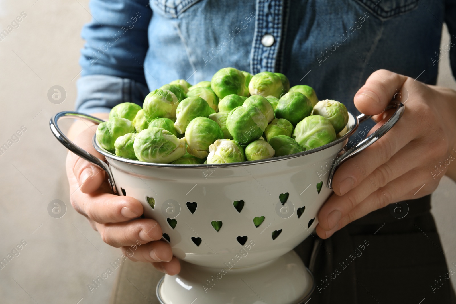 Photo of Woman holding colander with fresh Brussels sprouts, closeup