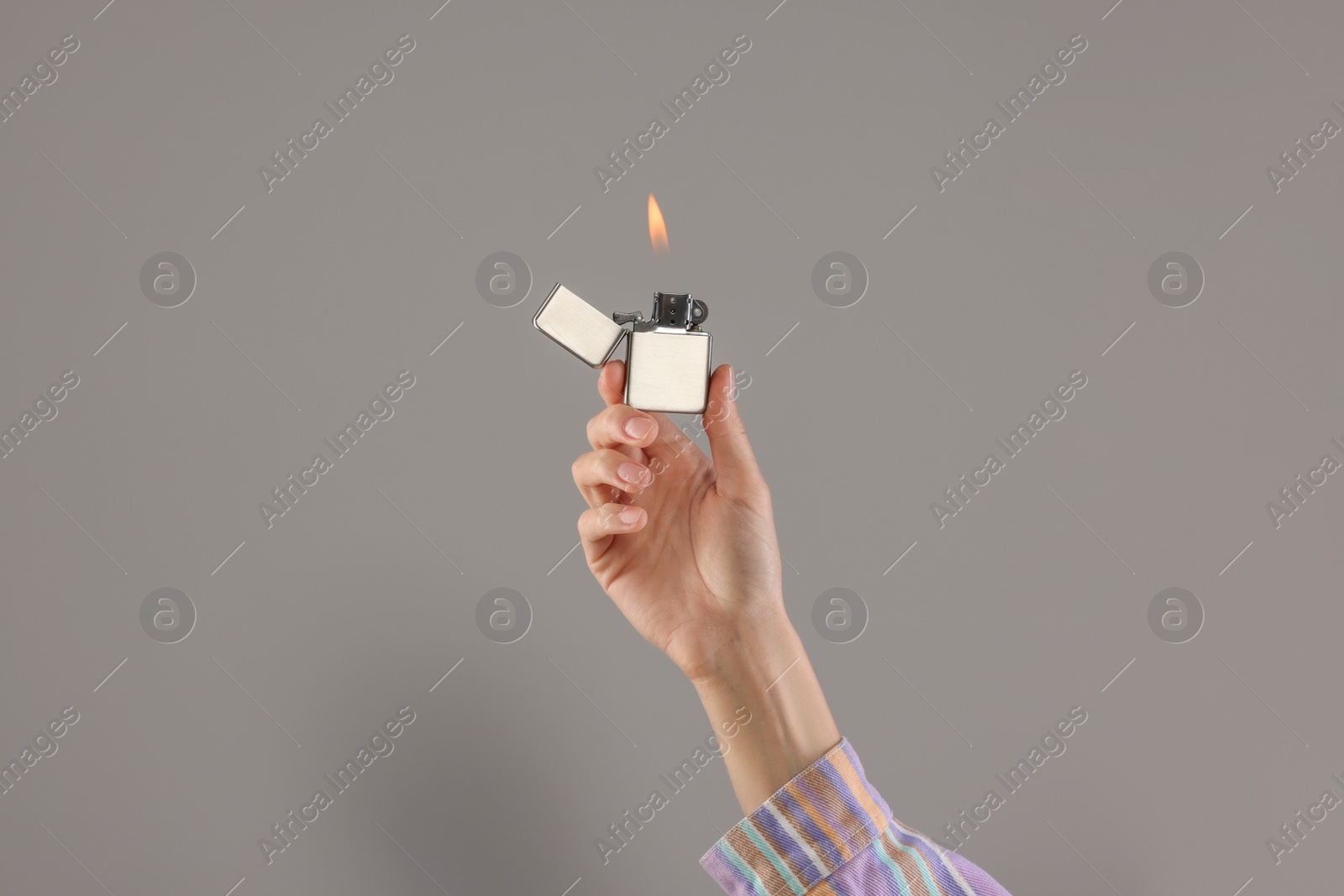 Photo of Woman holding lighter with burning flame on grey background, closeup