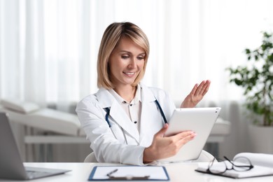 Photo of Smiling doctor with tablet having online consultation at table in office