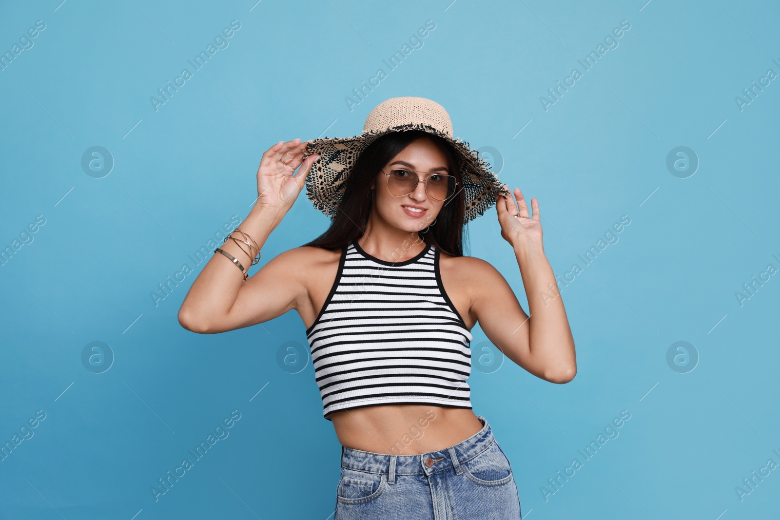 Photo of Beautiful young woman with straw hat and stylish sunglasses on light blue background