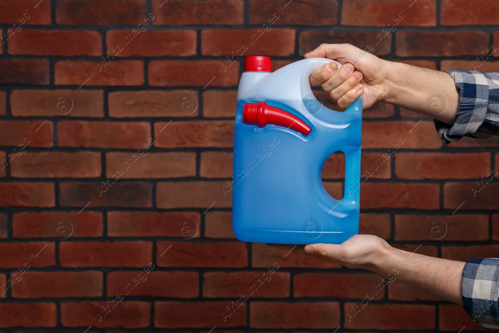 Photo of Man holding canister with blue liquid near brick wall, closeup. Space for text