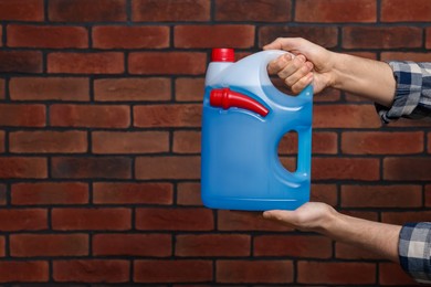 Man holding canister with blue liquid near brick wall, closeup. Space for text