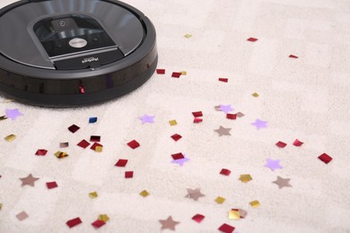 Modern robotic vacuum cleaner removing confetti from carpet. Space for text