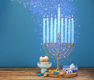 Image of Hanukkah celebration. Menorah with burning candles, dreidels, gift box and donuts on wooden table against light blue background, space for text