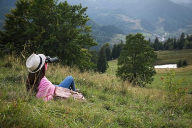 Young woman with binoculars enjoying mountain landscape. Space for text