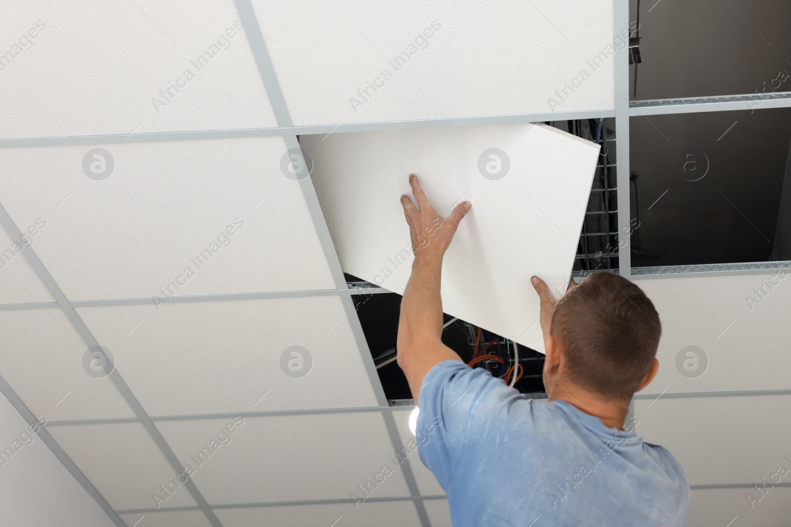 Photo of Suspended ceiling installation. Builder working with PVC tile, low angle view