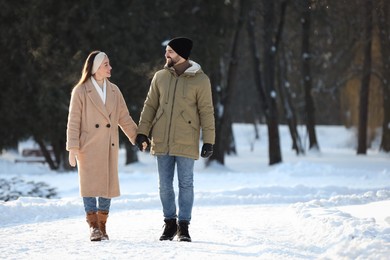 Happy young couple walking in snowy park on winter day