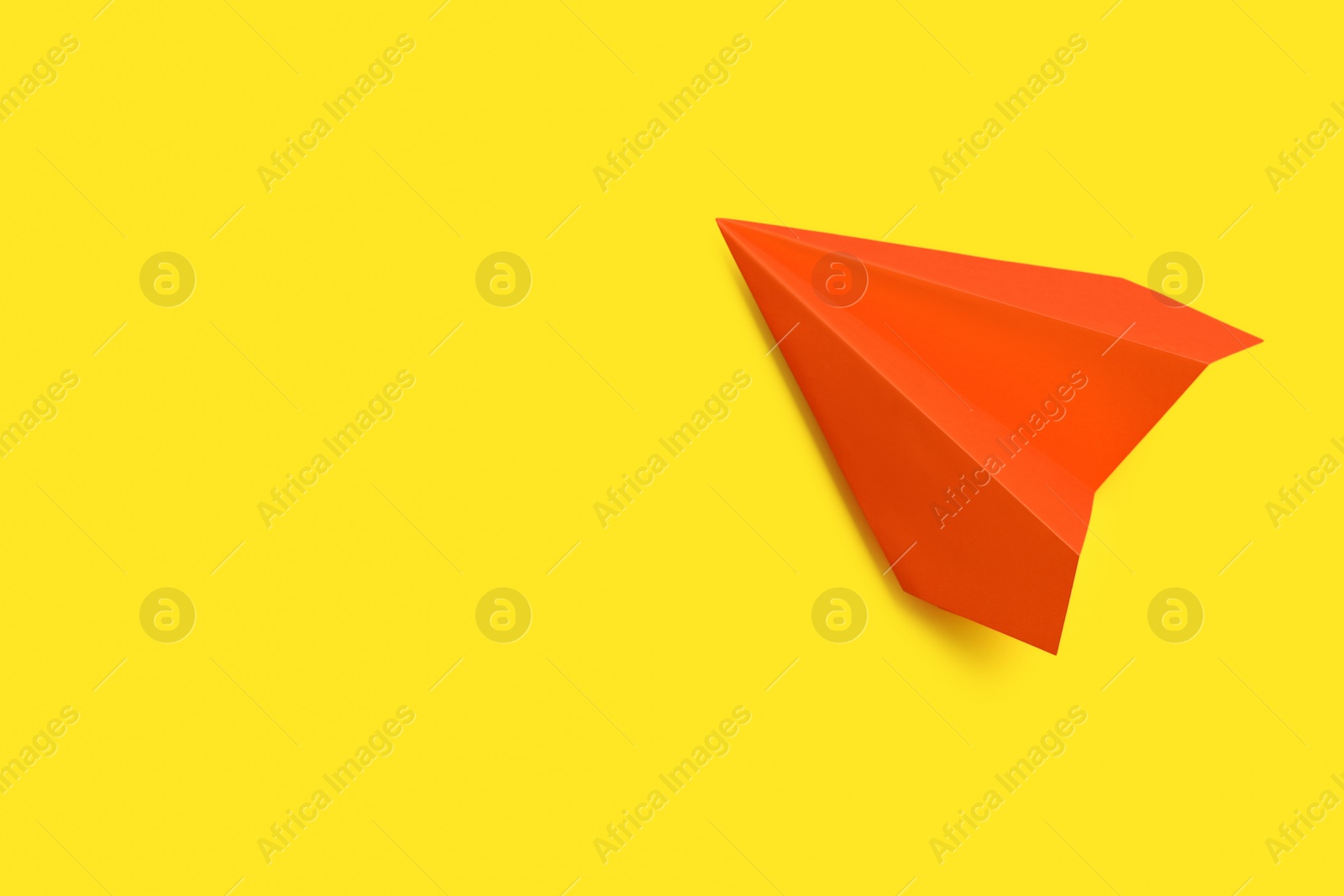 Photo of Orange paper plane on yellow background, top view. Space for text